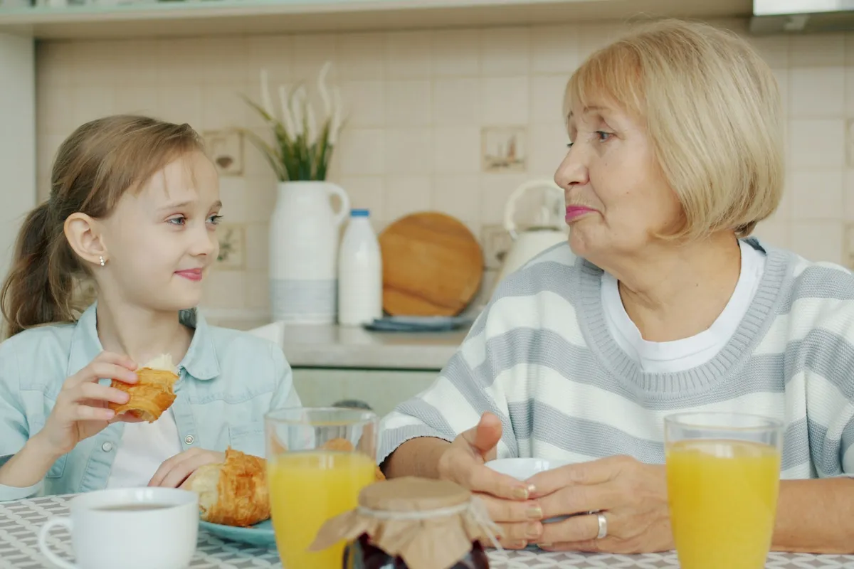 A grandmother and her granddaughter laughing together over breakfast.