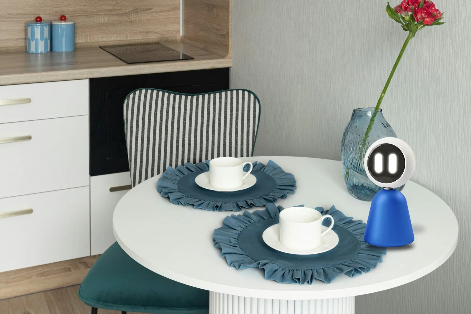 Tilly on a small round kitchen table beside a cup and a vase with a red flower.