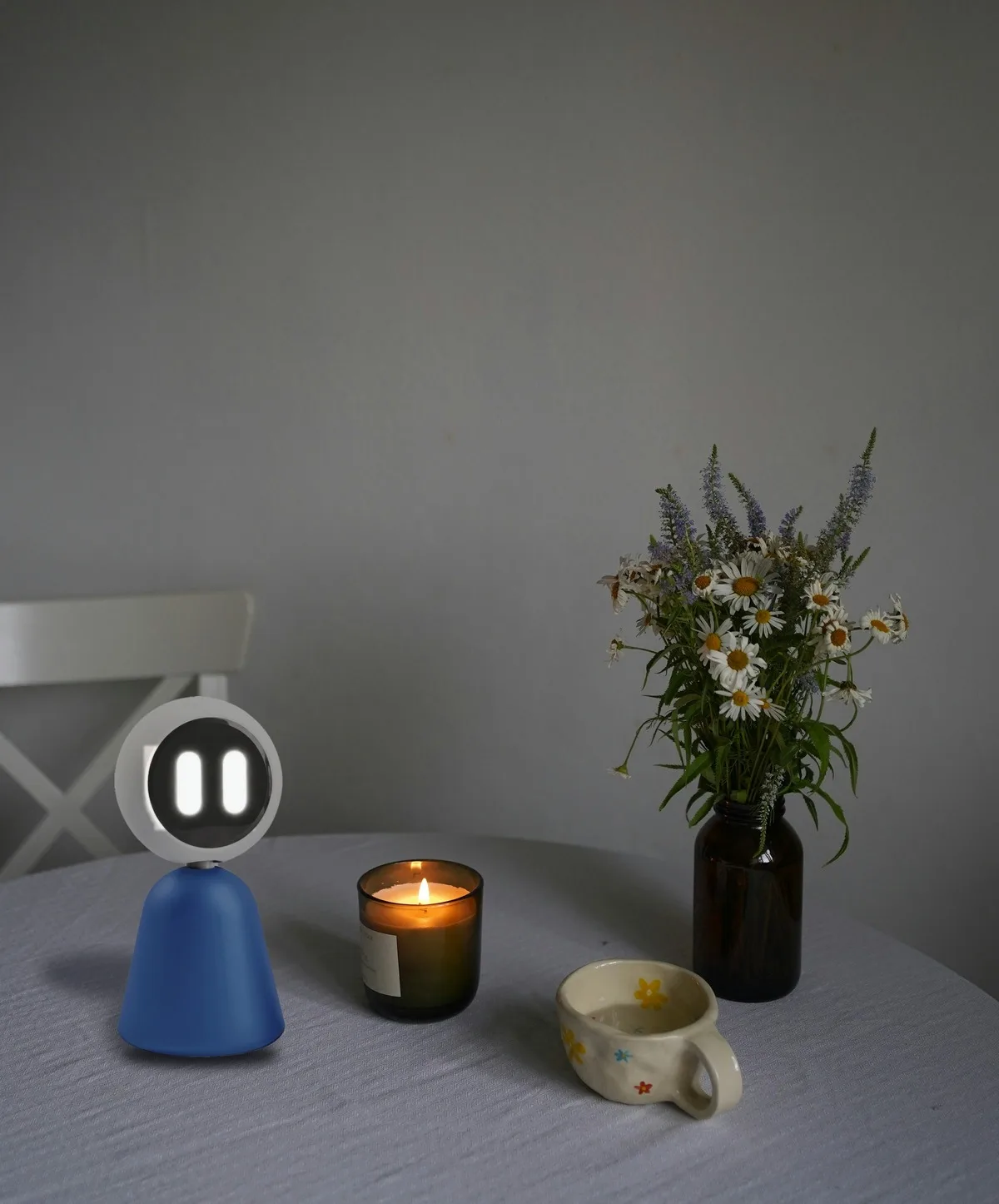 Tilly on a grey table next to a candle, a cup and a vase of wild flowers.